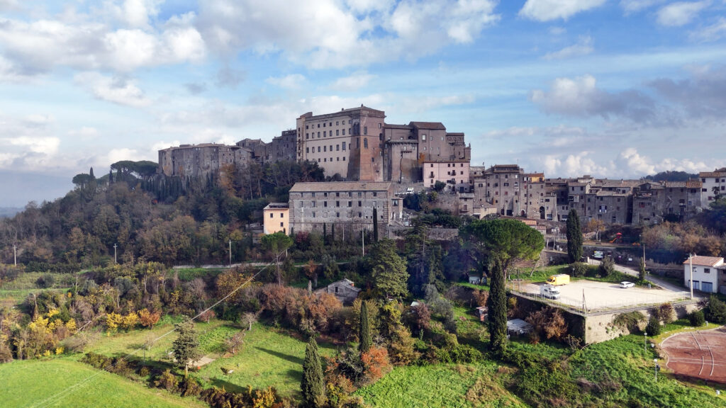 Centro storico di Bomarzo con Palazzo Orsini, circondato da colline boscose e campi verdi.