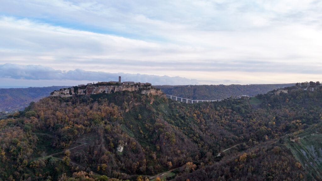 Civita di Bagnoregio su un altopiano di tufo al tramonto, con vista sulla stretta passerella che attraversa la valle profondamente incisa.