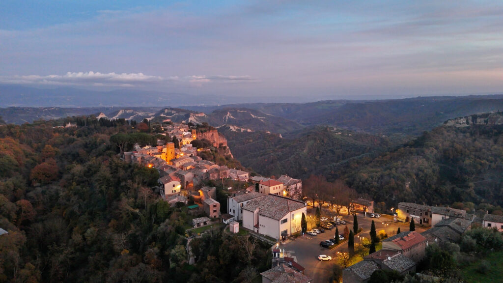 Veduta di Lubriano al tramonto, con il centro storico illuminato di arancione e un panorama sulla gola fino a Civita di Bagnoregio in lontananza.