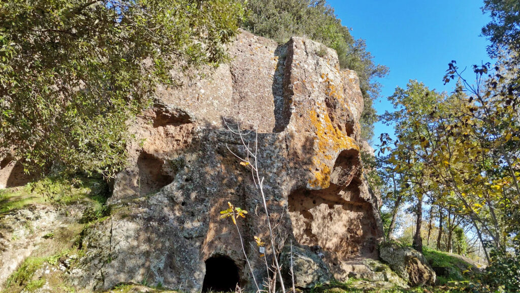 Detailed view of an Etruscan tomb carved into the tuff in Necropoli di Castel d'Asso, surrounded by trees and autumnal vegetation.