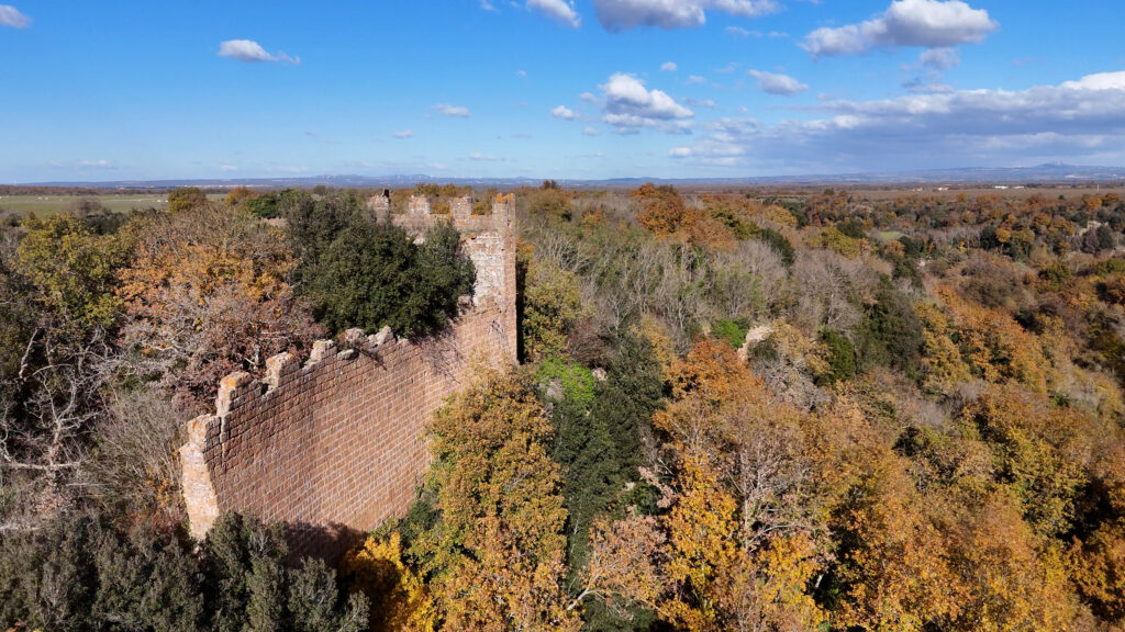 Drone shot of the castle of Norcchia, half hidden in the autumn coloured forest, with a wide view over the plain of Lazio.
