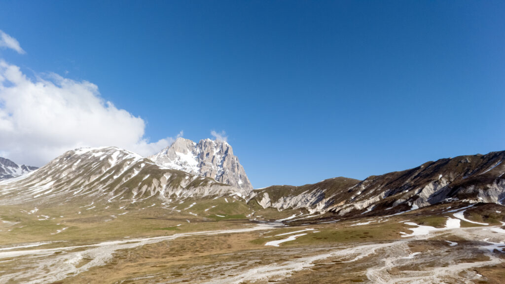 Blick über das Hochplateau von Campo Imperatore mit schneebedeckten Hängen und dem markanten Gipfel des Corno Grande unter klarem, tiefblauem Himmel.