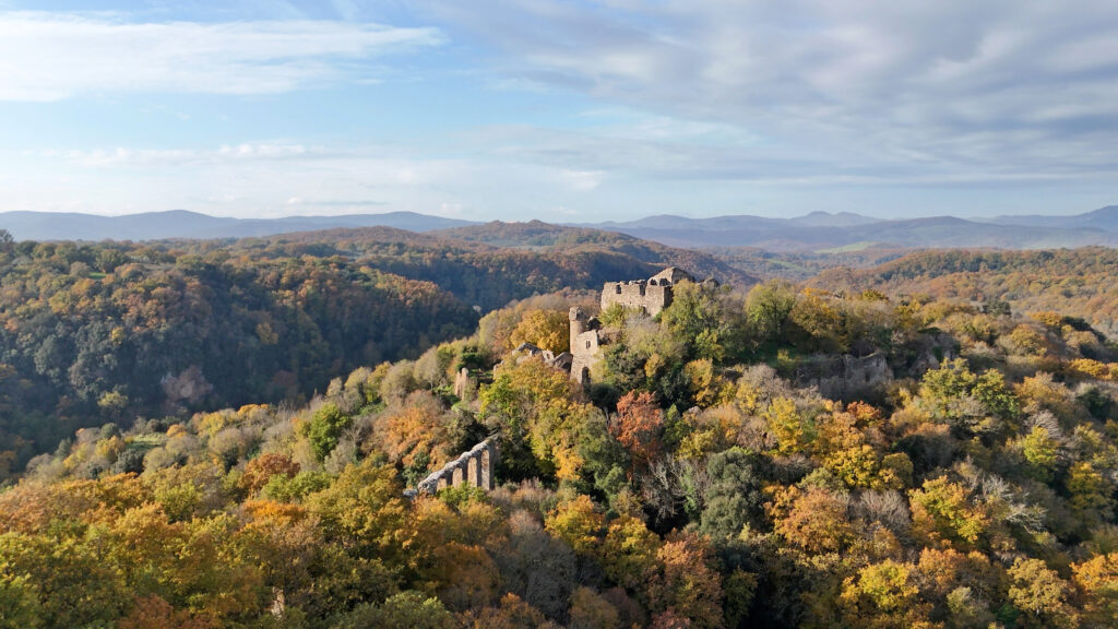 Drone view of the Monterano ruins on a forested hilltop surrounded by vibrant autumn colors.