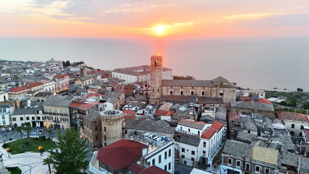 Drone shot of Vasto’s historic center at sunrise with the sun rising directly behind the bell tower of San Giuseppe and the Adriatic Sea in the background.