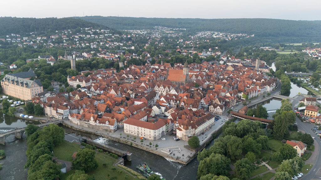 Wide aerial view of Hann. Münden’s old town at dusk with rivers, half-timbered houses, and green surroundings