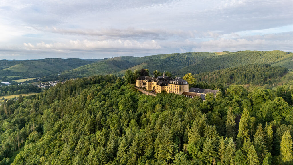 Wittgenstein Castle illuminated by warm evening light, surrounded by green forests and hills near Bad Laasphe in Germany.