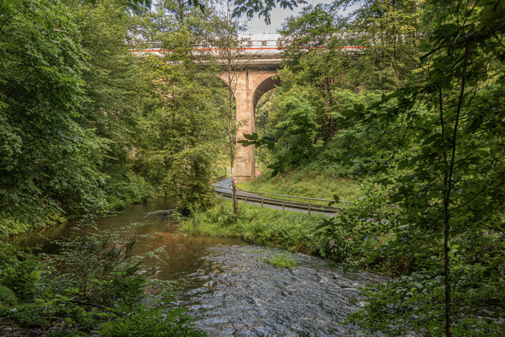 A historic sandstone railway bridge crossing the Aubach, where engineered structure meets the quiet flow of the Spessart forest.