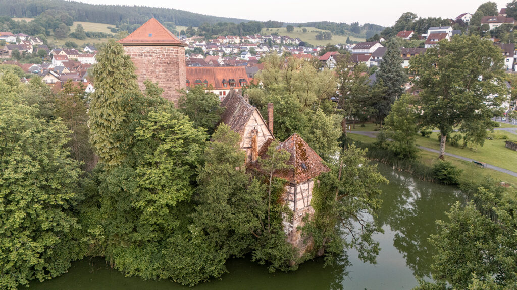 Aerial view of historic castle buildings and tower of Burgsinn surrounded by trees and water in Lower Franconia, Bavaria, Germany