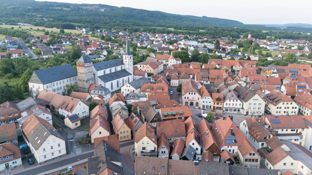 Aerial view of Bischofsheim in der Rhön showing the historic town centre with St. George’s Church, red rooftops and the surrounding Rhön landscape in Lower Franconia, Germany.
